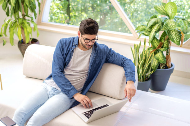 自信的男人坐在沙发上，在家里用笔记本电脑图片下载