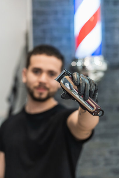 一个理发师在他的理发店里向镜头展示一个理发器的垂直肖像。专注于机器。图片下载