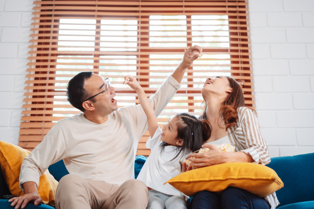 亚洲家庭由父母和女儿在家里客厅的沙发上看电视或电影，吃爆米花组成。享受放松的快乐。图片下载