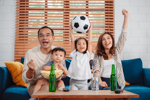亚洲家庭和女儿在家里客厅的沙发上看体育比赛，欢呼，兴奋地吃爆米花。享受放松的快乐。图片下载