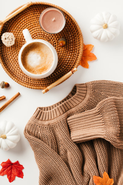 秋天的氛围。以藤盘、咖啡杯、蜡烛、棕色针织衫、白底枫叶等平铺构图图片下载