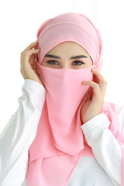 漂亮的年轻亚洲阿拉伯妇女戴着穆斯林粉红色的头巾在工作室自信。孤立的白色背景肖像与美丽的眼睛女孩。她抚摸着自己的脸。广告肖像概念。图片下载