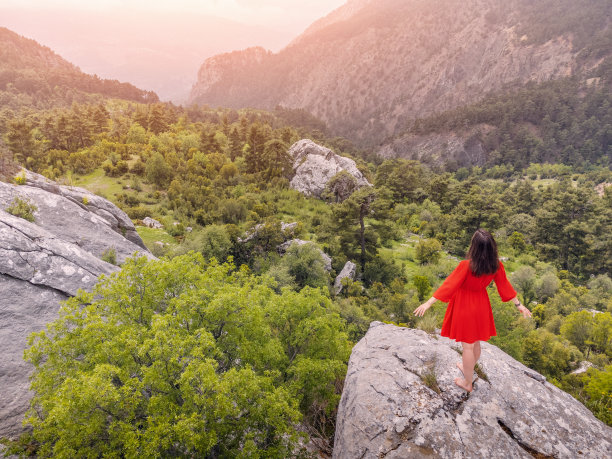 浪漫的航拍照片，一个女孩穿着红色的裙子，站在悬崖顶上，欣赏着山间峡谷的景色图片下载