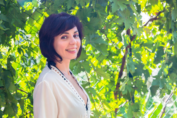 一个美丽的黑发女人的肖像，穿着浅色的夏季连衣裙，靠近绿色植物图片下载