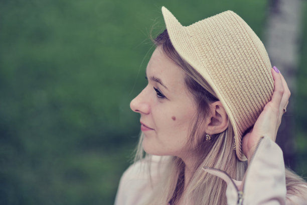 一个戴着帽子的女人的侧视图，在她的脸颊上显示出她独特的胎记，为她的外表增添了个性。拥抱个性和独特的美丽特质图片下载