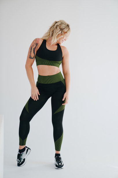 一位身穿黑绿运动服的迷人金发女郎在白色背景上摆姿势。图片下载