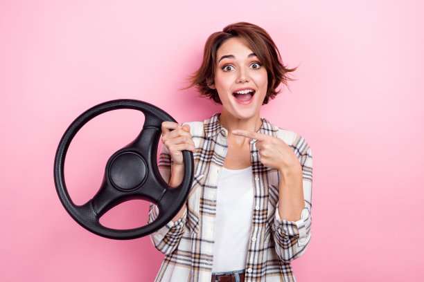 照片的兴奋时髦的女士穿格子夹克指向手指方向盘孤立的粉红色背景图片下载