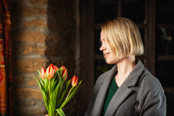 穿大衣的女人拿着一束深色背景的郁金香。假期,礼物。图片下载