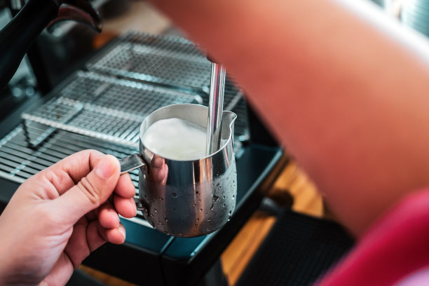 专业咖啡师为卡布奇诺热牛奶。咖啡师使用咖啡机制作拿铁咖啡的手图片下载