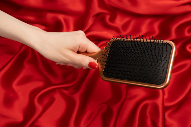 女人手里拿着一把红色的发刷，红色的指甲在红色的背景上。图片下载