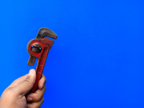 男人拿着一个古老而质朴的小管钳或猴子钥匙。一种用于家庭管道的工具。蓝色背景隔离图片下载