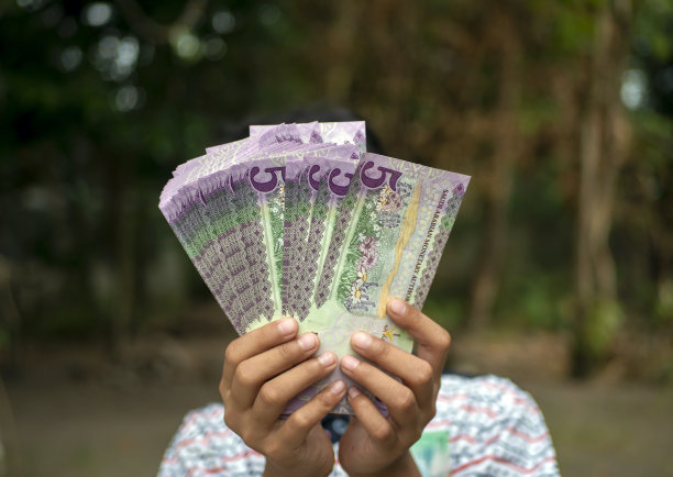 亚洲孩子手里拿着五里亚尔，这是沙特阿拉伯的货币，象征着给予和慈善的概念图片下载