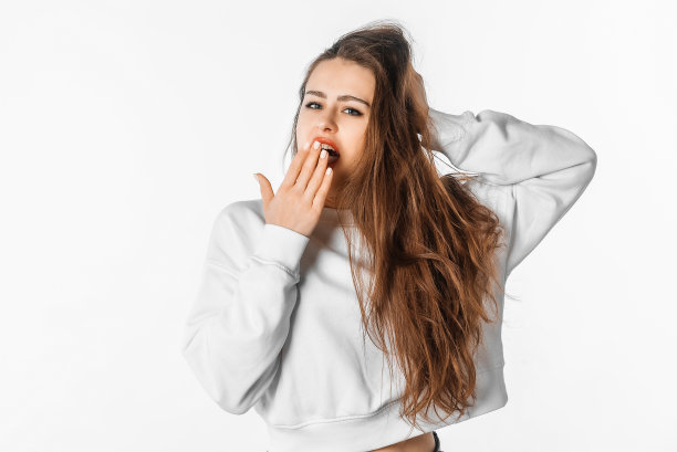 昏昏欲睡的年轻女子在打哈欠时捂着嘴。疲惫的黑发女性无聊地打着哈欠，在白色的工作室背景下摆姿势图片下载