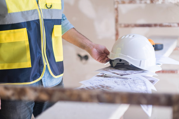 身穿背心的建筑师戴着白色头盔，在一堆项目文件上继续装修图片下载