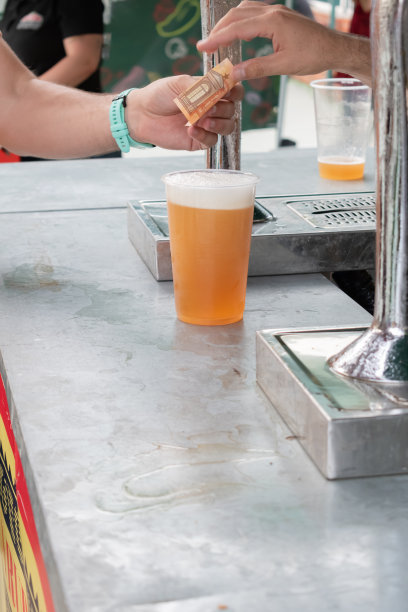 一个女人在街边摊上给一个男人买啤酒。夏季街头节日。图片下载