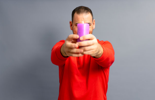 40多岁的西班牙裔男子，身穿一件红色套头衫，脸上点着一根紫色的蜡烛，孤立在灰色的工作室背景中。图片下载