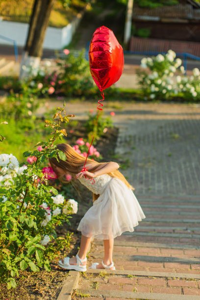 穿白裙子的金发女孩，手拿红气球。夏天的生活方式。童年图片下载