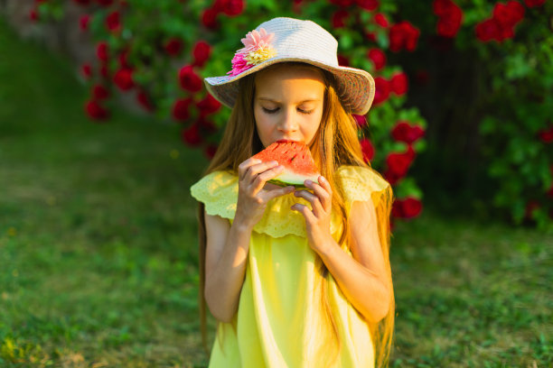 快乐的金发女孩穿着黄色的衣服，拿着一块西瓜。夏天的生活方式。的童年。图片下载