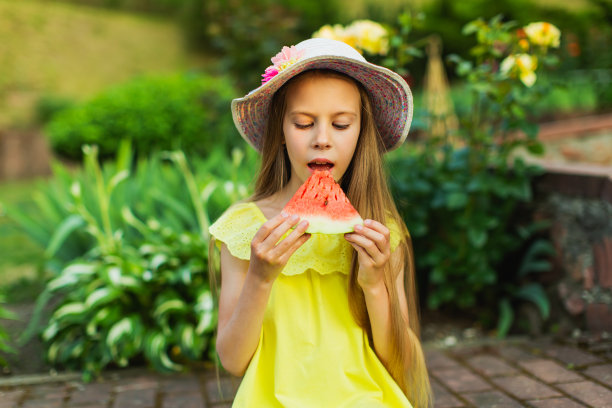 快乐的金发女孩穿着黄色的衣服，拿着一块西瓜。夏天的生活方式。的童年。图片下载