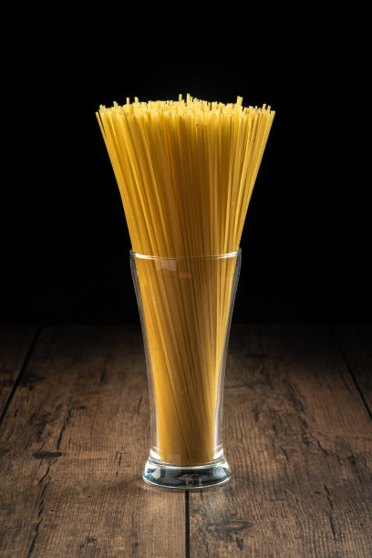 意大利面被放在一个准备在木桌上烹饪的玻璃杯里。图片下载