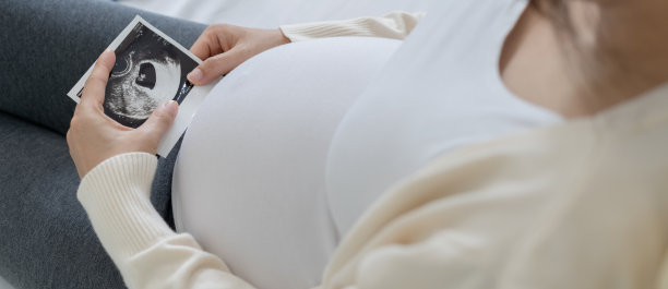 一位孕妇正在看胎儿的超声波照片。妈妈轻轻地摸了摸婴儿的肚子。快乐，家庭，成长，怀孕，享受，准备新生儿，照顾，保健，肚子。图片下载