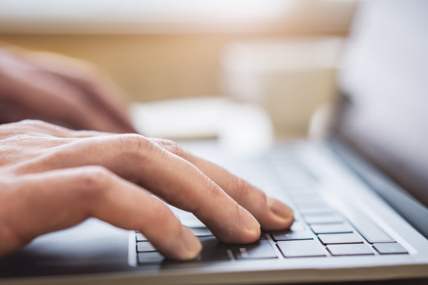 这张照片的特写是男性的手在当代笔记本电脑的键盘上打字，背景是模糊的办公室场景图片下载