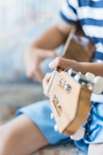 一个白人小孩在用小吉他或尤克里里琴演奏和弦图片下载