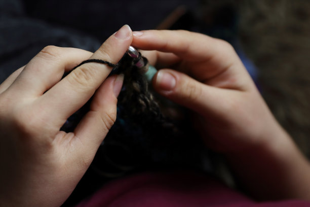 年轻的女士手里拿着钩针和毛线，制作手工套头衫，是在家放松时的手工爱好，为牛皮艺术或农贸市场制作独特的产品。图片下载