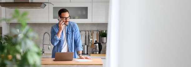 严肃的年轻商人在家里的厨房柜台上用智能手机和笔记本电脑讨论图片下载