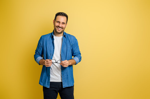 一个面带微笑的英俊商人，戴着眼镜，站在黄色的背景上图片下载