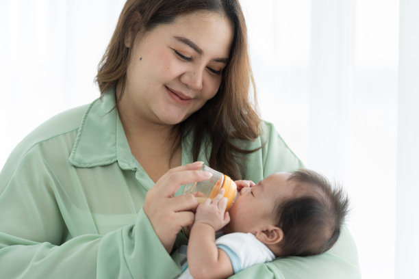 母亲抱着刚出生的婴儿用奶瓶喂奶。新生儿或婴儿在母亲拿着奶瓶时从乳头吃奶图片下载