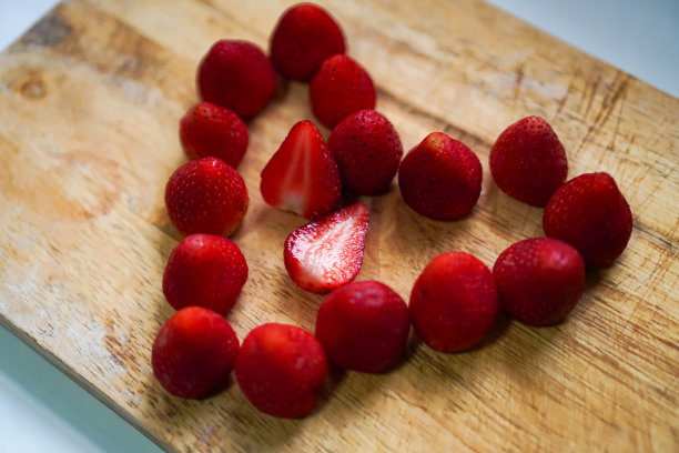图为在家里的餐桌上，摆放着有机草莓果肉和草莓果实的木托盘。图片下载