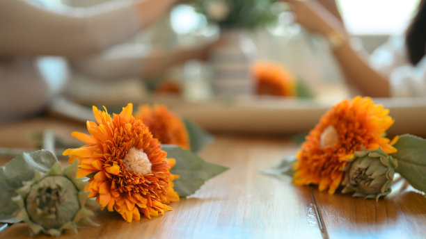 木桌上美丽的黄花的特写镜头，两个女人在背景上插花。图片下载