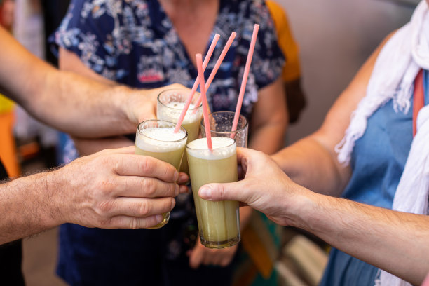 四个人拿着杯子，杯子里有装满甘蔗汁的粉红色管子。人们准备在果阿市场品尝绿色甜饮料。图片下载