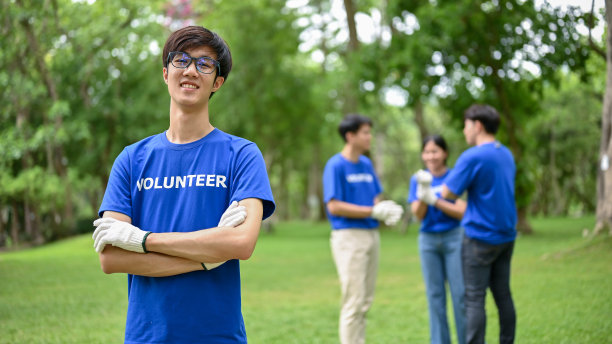 一位快乐的年轻亚洲男性志愿者站在公园里，双臂交叉图片下载