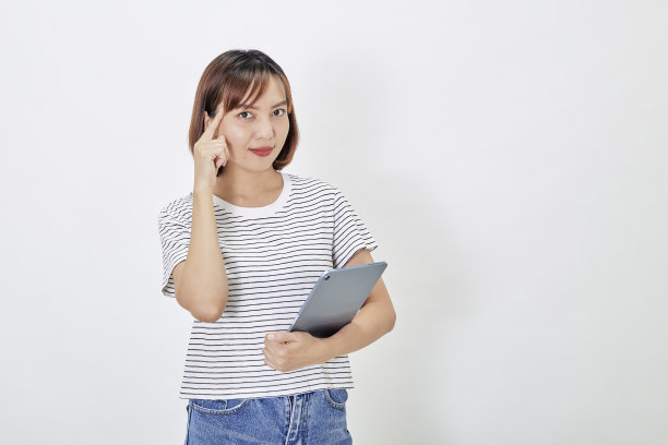 年轻的商业亚洲女雇员，棕色短发，穿着t恤和牛仔裤，微笑着，拿着电子平板电脑站在白色背景的复制空间图片下载