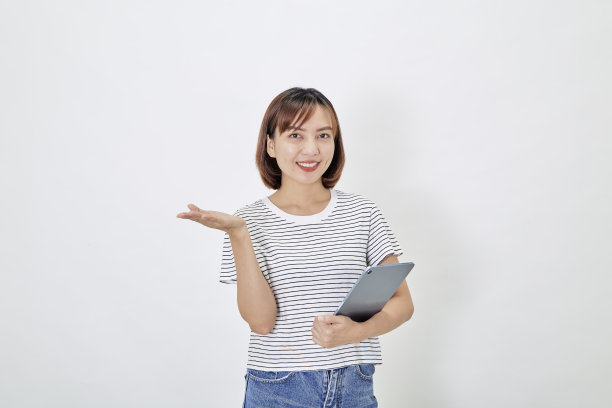 年轻的商业亚洲女雇员，棕色短发，穿着t恤和牛仔裤，微笑着，拿着电子平板电脑站在白色背景的复制空间图片下载