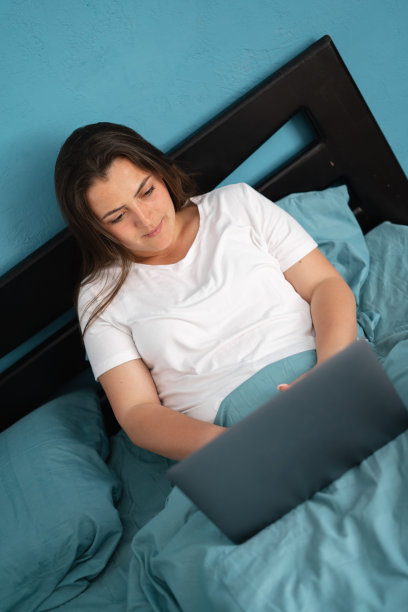 在家办公的女性在床上远程办公。使用电脑。远程教育和在线教育的工作理念图片下载