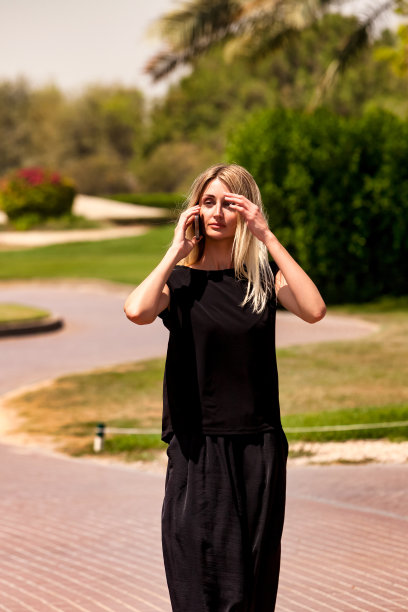 可爱的年轻女商人的肖像，穿着黑色衣服，在城市公园用手机打电话。非常苗条的金发商人在大自然中使用手机。休闲活动概念。复制广告文本空间图片下载
