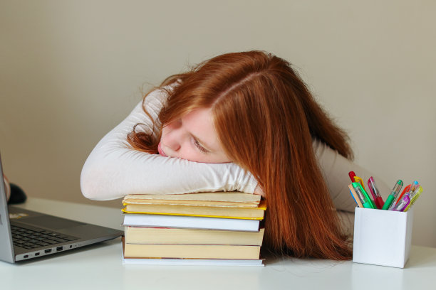 疲惫不堪的白人女学生坐在图书馆里拿着书闭上眼睛按摩她的头图片下载