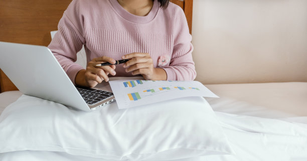 商务女记账员手里拿着笔，用笔记本电脑在床上做记帐纳税，在家办公的概念图片下载