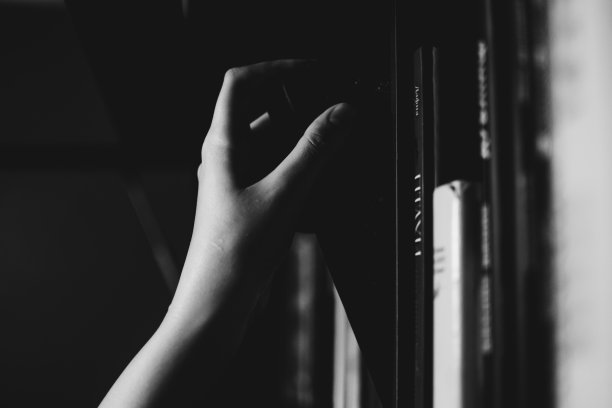 一个女孩苍白的手在书架上挑一本黑色的书。文学，阅读，识字和知识的概念。黑白电影图片下载