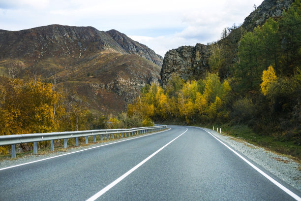 弯弯曲曲的柏油路，纵横于雪峰、黄沙、秋林、蓝天之间。汽车行驶在高速公路上，背景是山景图片下载