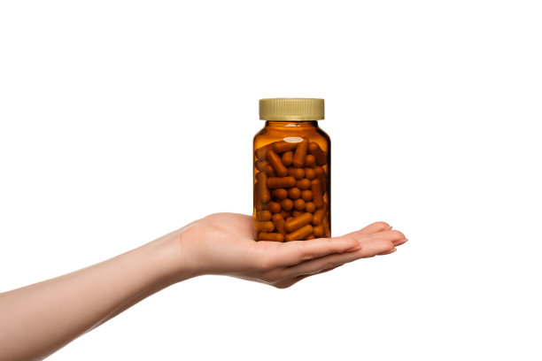 一张女性手拿着药瓶的照片，背景是白色的。半透明的棕色罐子，药丸清晰可见。图片下载
