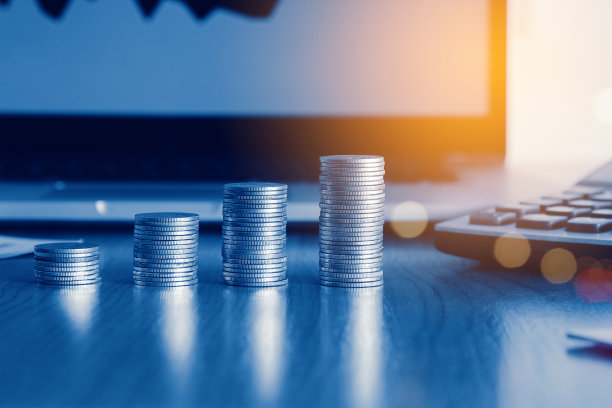 叠钱硬币用笔记本电脑打开交易图，金融投资概念用蓝色滤镜可以作为背景图片下载