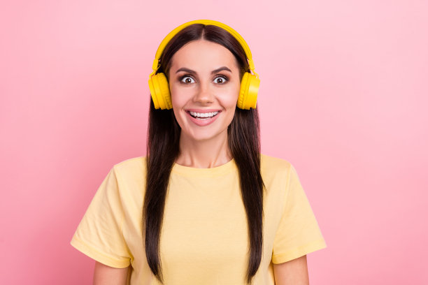 照片中兴奋时髦的女士穿着黄色t恤听着歌曲，耳机孤立的粉红色背景图片下载