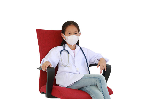 一个亚洲女孩，穿着白色的医生服，戴着防护面具，坐在红色的椅子上，与白色的工作室背景隔绝。图像与剪辑路径图片下载