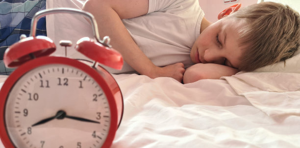 带着闹钟的可爱少年睡在床上图片下载