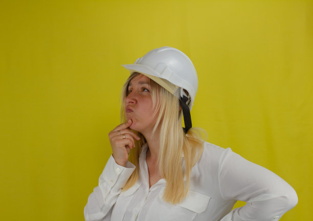 一个戴着建筑头盔的女工程师在黄色孤立的背景上用一种有趣的表情思考着。一位女工程师正在考虑建筑计划。图片下载