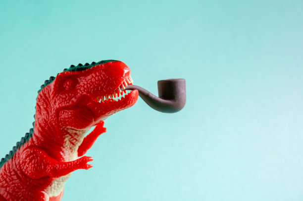 靠近红色恐龙与吸烟烟斗在蓝色背景。吸烟的概念。本空间图片下载